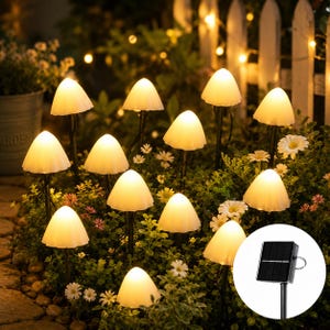 May include: A garden scene featuring mushroom-shaped solar lights with a warm, inviting glow. The lights are arranged among greenery and small white flowers, creating a whimsical ambiance. A solar panel is visible, indicating the lights' energy source.