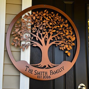 May include: A circular copper-coloured metal wall sign featuring a detailed tree silhouette with numerous leaves. The base of the sign includes the text "THE SMITH FAMILY" and "EST 2026" in black lettering, mounted on a dark door surface.