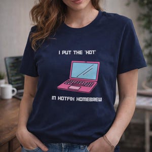 May include: Navy blue t-shirt with the text "I PUT THE 'HOT' IN HOTFIX HOMEBREW" above a pink and blue laptop graphic. The shirt is a short-sleeved crew neck.
