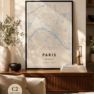 Op de afbeelding: Een ingelijste verticale wandkunstprint met een gedetailleerde kaart van Parijs, Frankrijk. De kaart toont blauwe waterwegen tegen een beige achtergrond. Onder de kaart staat de tekst PARIS, FRANCE en de coördinaten 48.8566 N | 2.3522 E.
