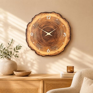 May include: A round wall clock featuring a natural wood grain slice design with a dark brown bark edge. The clock face displays white numerals at the 12, 3, 6, and 9 o'clock positions, with thin gold-colored hour and minute hands centered on the wood.