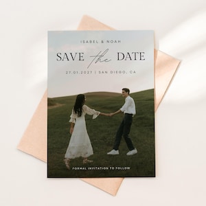May include: A rectangular Save the Date card featuring a photograph of two people holding hands in a grassy field. The text reads ISABEL & NOAH, SAVE the DATE, 27.01.2027 | SAN DIEGO, CA, and FORMAL INVITATION TO FOLLOW. The card rests on a light peach envelope.