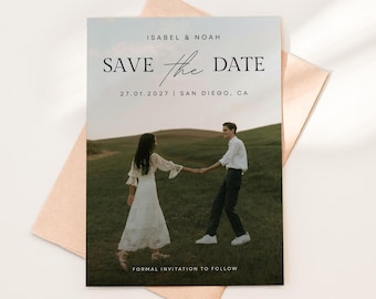 May include: A rectangular Save the Date card featuring a photograph of two people holding hands in a grassy field. The text reads ISABEL & NOAH, SAVE the DATE, 27.01.2027 | SAN DIEGO, CA, and FORMAL INVITATION TO FOLLOW. The card rests on a light peach envelope.
