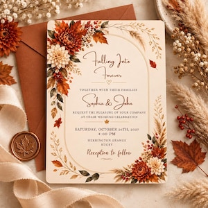 May include: A rectangular wedding invitation card featuring an arched frame decorated with autumn-themed illustrations of red and white dahlias, dried grasses, and maple leaves. The text reads Falling Into Forever, Sophia & John, and details.