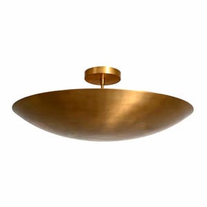 Può includere: Un apparecchio di illuminazione a soffitto a forma di ciotola, color oro. L'apparecchio ha un design a ciotola ampia e poco profonda e una piastra di montaggio circolare. La luce è realizzata in metallo e ha una superficie liscia e riflettente. L'apparecchio è progettato per essere montato a filo del soffitto.