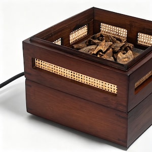 May include: A dark brown wooden incense burner with woven rattan accents. The square box-shaped burner has a top section filled with wood chips and a lower section with a woven pattern. A black power cord extends from the side.