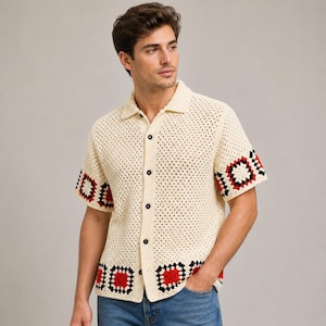 May include: Cream-colored crochet shirt with short sleeves and a button-down front. The shirt features black buttons and red and black geometric patterns on the sleeves and hem. The shirt is made of a breathable, open-weave fabric.