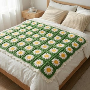 Pode incluir: Um cobertor de crochê feito à mão com um padrão de margaridas. O cobertor tem um fundo verde com flores de margarida brancas e amarelas. As bordas são finalizadas com uma borda branca com vieiras. O cobertor é exibido em uma cama com lençóis brancos e almofadas bege.