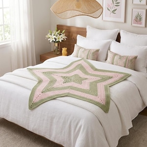 Può includere: Una coperta all'uncinetto a forma di stella, nei toni del rosa e del verde, poggia su un letto bianco. La coperta è il punto focale, con un design a stella a cinque punte. La camera da letto ha una palette di colori neutri con biancheria da letto bianca e mobili in legno.