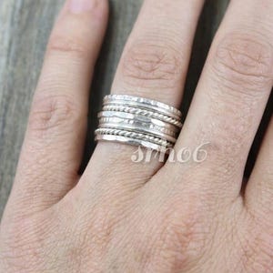 May include: A stackable silver ring set consisting of five individual bands worn together. The set features a combination of smooth, hammered, and twisted rope-textured bands in a polished metallic finish, creating a layered appearance.