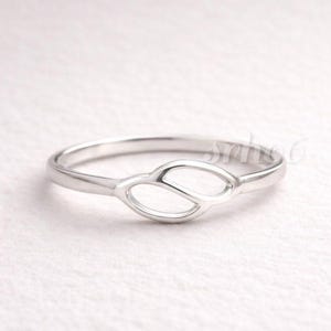 May include: A polished silver ring featuring a central openwork design composed of two interconnected, leaf-shaped loops. The band is smooth and slender, showcasing a metallic finish that reflects light across its curved surface.
