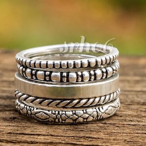 May include: A stack of five silver rings featuring varied textures including a beaded band, a smooth polished band, a twisted rope design, and a band with an embossed pattern. The word srhog is visible in white text overlaid on the rings.