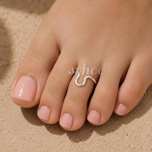 Puede incluir: Un anillo para el dedo del pie de color plateado con un diseño ondulado o serpentino suave y continuo. La banda de metal se curva en una forma suave y redondeada que rodea el segundo dedo. La superficie del anillo tiene un acabado pulido.