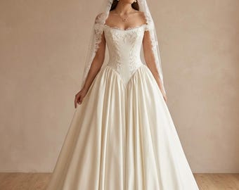May include: An off-white floor-length gown with an off-the-shoulder neckline and a fitted bodice featuring intricate white embroidery. The skirt is full and voluminous with a smooth satin finish. A long, sheer lace-trimmed veil covers the head.