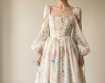 Könnte beinhalten: Ein bodenlanges Kleid in Off-White mit einem zarten Blumenmuster in Rosa-, Blau- und Grüntönen. Das Kleid hat einen eckigen Ausschnitt, lange Puffärmel mit Bindebändern an den Manschetten und eine durchgehende Knopfleiste auf der Vorderseite.