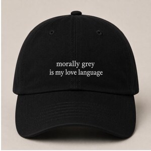 May include: Black baseball cap with the phrase "morally grey is my love language" in white lettering. The cap has a curved brim and a button on top. A casual accessory for everyday wear.