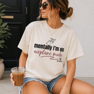 May include: A cream-coloured t-shirt featuring the text "mentally I'm on airplane mode" in black and burgundy. A small airplane graphic is above the text. The shirt also has the words "NO SIGNAL" below the main text.