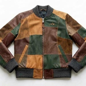 May include: A patchwork bomber jacket featuring a multi-coloured design of brown, tan, and dark green leather panels. The jacket includes a dark grey ribbed collar, cuffs, and hem, a front zip closure, two side pockets, and a small mountain logo.