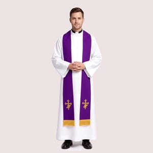 May include: A white robe with a purple stole featuring gold crosses and fringe. The collar is black. The person is wearing black shoes.