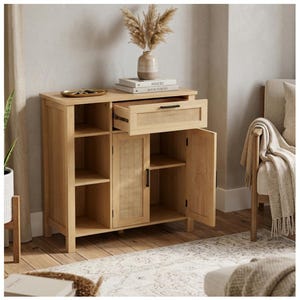 May include: A light wood cabinet with open shelves, a drawer, and a door. The drawer and door feature woven cane detailing. The cabinet is topped with a tray, books, and a vase with dried flowers. The cabinet is in a room with a rug and a chair.