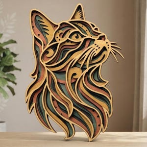 May include: A multi-layered wooden cat head wall art piece featuring intricate cutouts and a color palette of yellow, teal, and orange. The design displays a stylized feline profile with detailed whiskers and ears, showcasing depth through stacked layers.