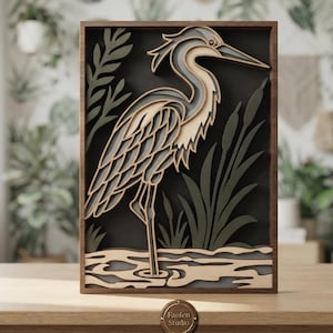 May include: A rectangular wooden wall art piece featuring a multi-layered laser-cut design of a heron standing in water among reeds. The artwork uses shades of beige, gray, and dark green, framed in dark wood. A small circular plaque reads Fanfen Studio.