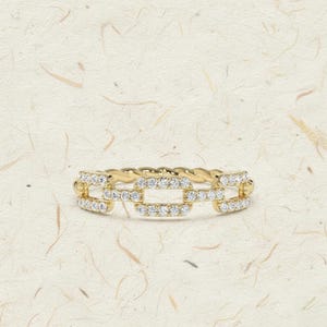 May include: A gold ring with a chain link design, encrusted with small, sparkling white gemstones. The band has a twisted rope texture. The ring is set against a light, textured background.