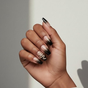 Peut inclure: Une main montre de longs faux ongles en forme de cercueil. Les ongles présentent un dégradé noir à nude. Un ongle a un motif de serpent doré à paillettes. Les ongles sont un accessoire élégant.