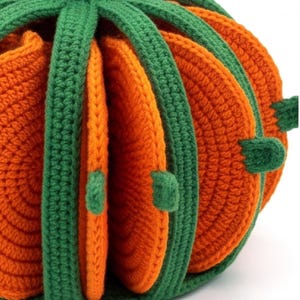 May include: A pumpkin-shaped holder made of orange and green yarn, featuring a series of circular orange crochet coasters stored vertically within green crochet dividers that form the exterior structure of the pumpkin shape.