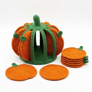 May include: A crochet pumpkin-shaped holder in green with orange pumpkin-shaped coasters. The holder features a ribbed structure with a central opening to store the circular orange coasters, each detailed with a small green stem accent.