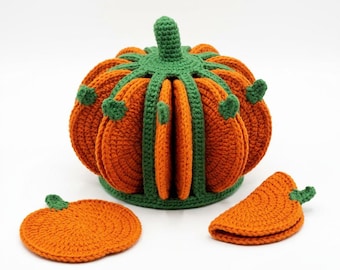 May include: A crochet pumpkin-shaped holder containing several orange circular coasters with green stems. The holder features a green ribbed structure that keeps the coasters upright. Two additional orange pumpkin-shaped coasters are placed in front.