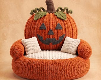 May include: A large, round, orange crocheted pumpkin-shaped chair with a brown stem and green leaves. The backrest features a dark gray jack-o'-lantern face. The seat is cream-colored with two small, matching cream-colored square throw pillows.