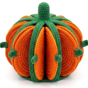 May include: A crocheted pumpkin-shaped object constructed from multiple orange circular segments separated by green vertical ribs. The structure features a central green stem at the top and small green protrusions extending from the sides of the orange panels.