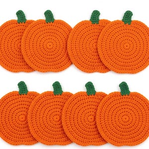 May include: A set of eight circular orange crochet coasters, each featuring a small green stem at the top. The coasters are arranged in two rows of four, showcasing a consistent round, textured stitch pattern throughout the orange pumpkin-shaped bodies.