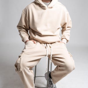 Peut inclure: Ensemble de survêtement beige composé d'un sweat à capuche et d'un pantalon cargo assorti. Le sweat à capuche a une capuche à cordon et une poche avant. Le pantalon de survêtement a des poches cargo et une taille à cordon.