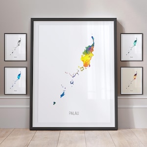 May include: A series of framed art prints depicting Palau. The central print displays a vibrant watercolour map of Palau, with the word "PALAU" beneath. Surrounding prints show monochrome and colour variations of the same map. The prints are on a wooden floor.