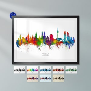 Pode incluir: Uma impressão de arte de parede emoldurada com uma silhueta colorida em aguarela do horizonte de Munique. A obra exibe vários edifícios da cidade em tons vibrantes de vermelho, amarelo, verde e azul sobre um fundo branco com o texto MUNICH - DEUTSCHLAND.