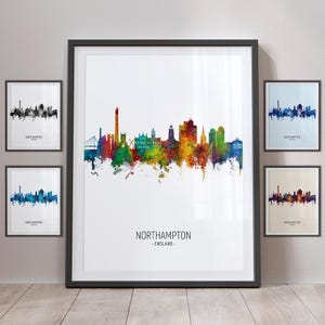 Op de afbeelding: Een ingelijst afdruk van een kleurrijk aquarel stadsbeeld van Northampton, Engeland. De skyline is afgebeeld in tinten blauw, groen, geel, oranje en rood. De naam van de stad en de locatie zijn onder de skyline afgedrukt.