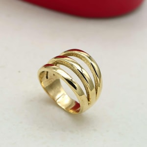 Peut inclure: Une bague dorée présentant un design à trois anneaux. La bague se compose de trois bandes parallèles, lisses et polies, réunies à la base pour former un seul bijou cohérent avec une finition métallique réfléchissante et brillante.