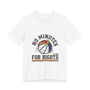 Puede incluir: Camiseta blanca con un diseño gráfico que presenta una pelota de baloncesto en colores arcoíris, con el texto "NO MINUTES FOR BIGOTS". El diseño incluye una franja de color arcoíris en la parte inferior.