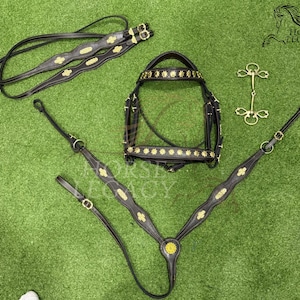 Könnte beinhalten: Ein schwarzes Leder-Pferdezaumzeug-Set mit goldfarbenen floralen Akzenten. Das Set enthält einen Kopfstück, Brustblatt, Zügel und Gebiss, alles auf einer grünen Oberfläche angeordnet. Das Horse Legacy-Logo ist sichtbar.