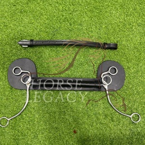 May include: A black leather horse bit with silver metal rings and a leather strap. The bit has a curved design. The brand name "HORSE LEGACY" is visible. The item is set against a green background.