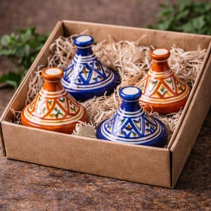 May include: Four miniature, colorful tagine pots in a cardboard box. The tagines are blue and orange with geometric patterns. The box is filled with straw. The Atlas Handmade logo is in the top left corner.