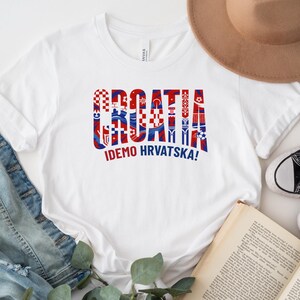 a white t-shirt with a graphic design, a hat, a pair of jeans, a book, and some sneakers.