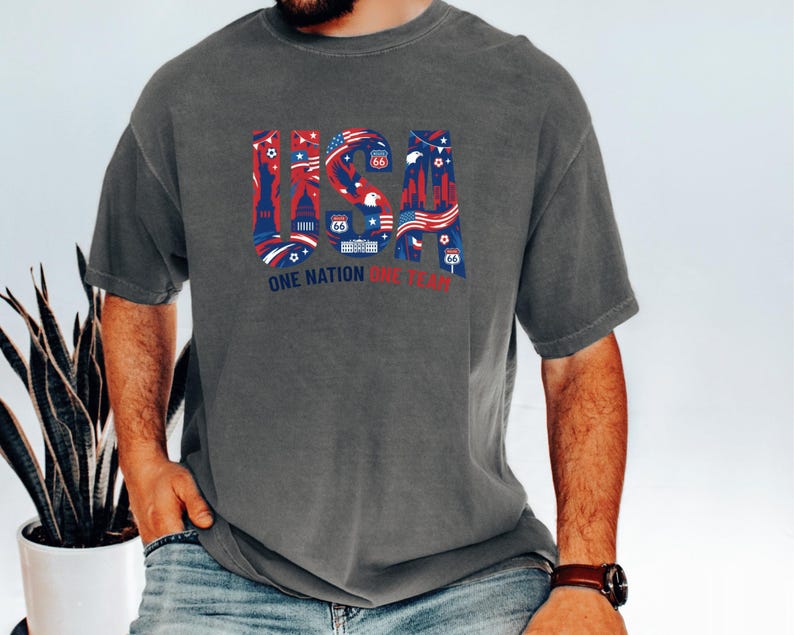 A man wearing a gray t-shirt with a graphic design of the United States and the text "One Nation, One Team" printed on it.