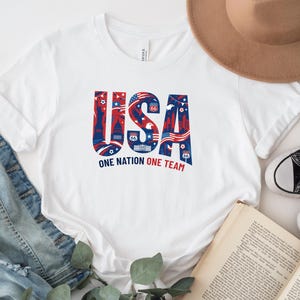 a white t-shirt with a patriotic design, a hat, a pair of jeans, a book, and some sneakers.