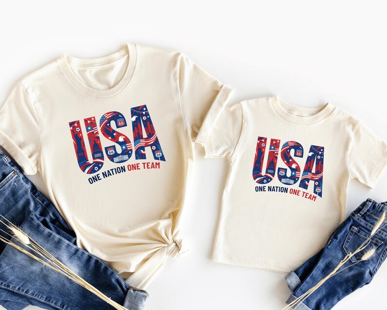 two white t-shirts with the text "USA" printed on them, along with a pair of blue jeans.