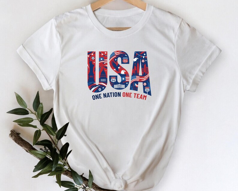 A white t-shirt with the text "USA" and "ONE NATION ONE TEAM" printed on it, along with various patriotic symbols and designs.