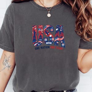 A person wearing a gray t-shirt with a graphic design featuring various symbols and text related to the United States.