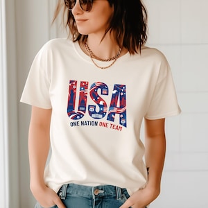 A woman wearing a white t-shirt with the text "USA" and "ONE NATION ONE TEAM" printed on it.